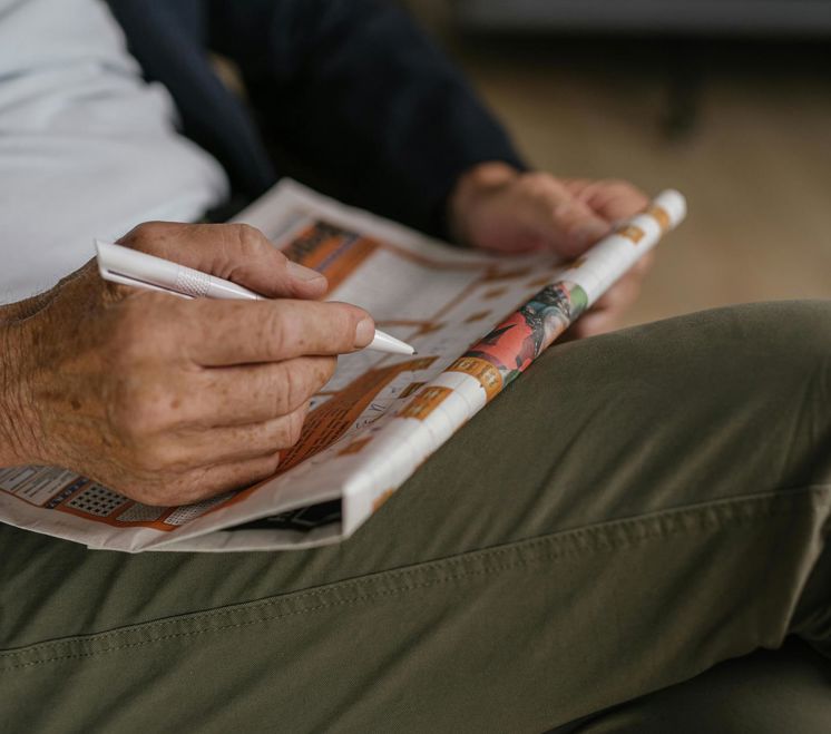 Eine Person löst ein Kreuzworträtsel in einer Zeitung