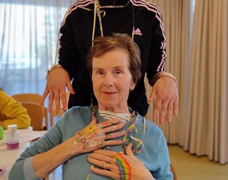 Eine Bewohnerin mit Blumen und Regenbögen auf den Händen und die stolze junge Frau, die sie gemalt hat